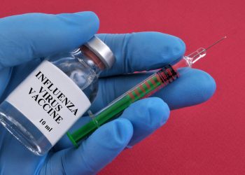 Influenza vaccine concept with vial and syringe in latex gloved hand on red background