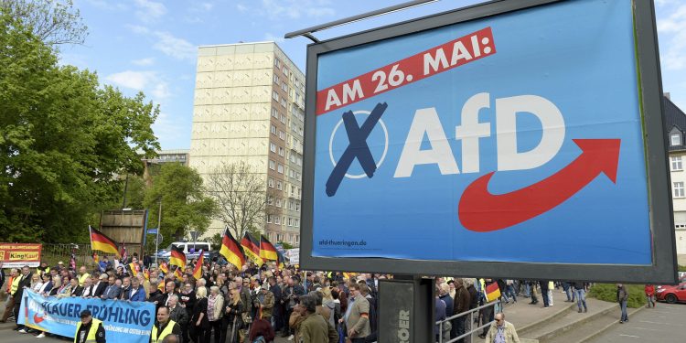 File---File picture taken May 1, 2019 shows AfD supporters walkin along a party elections poster in Erfurt, Germany. German media outlets are reporting the country's domestic intelligence agency has put the opposition Alternative for Germany party under observation under suspicion of extreme right sympathies. (AP Photo/Jens Meyer, file)